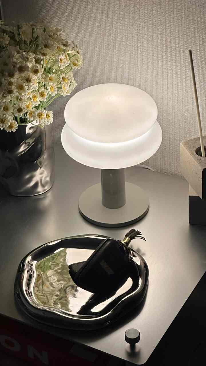 White-toned table featuring a white table lamp, black vase with flowers, and silver tray creating a simple setting