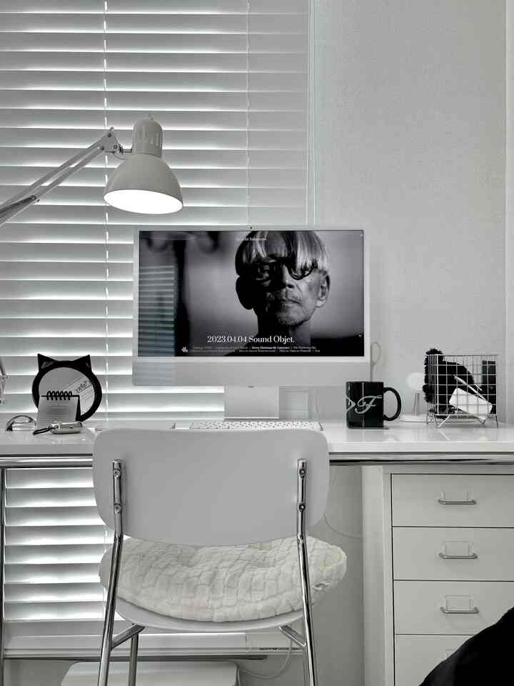 Compact home office in white and black monotone featuring a white desk, chair, Ikea lamp, and a black cat in a tidy workspace