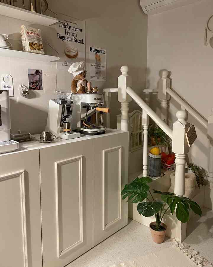 ホワイトとベージュの色調のキッチン空間、キャビネット上のホームカフェ機器と壁のポスターが配された雰囲気のあるインテリア