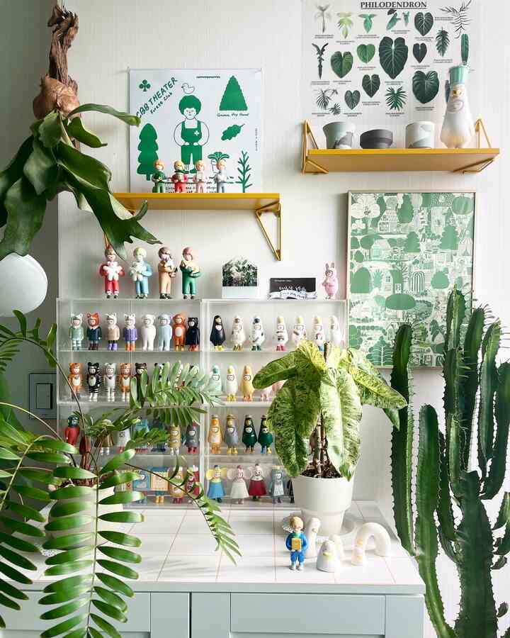 Bright white-walled kitchen space with tiled surface featuring various green plants and collectible figurines displayed