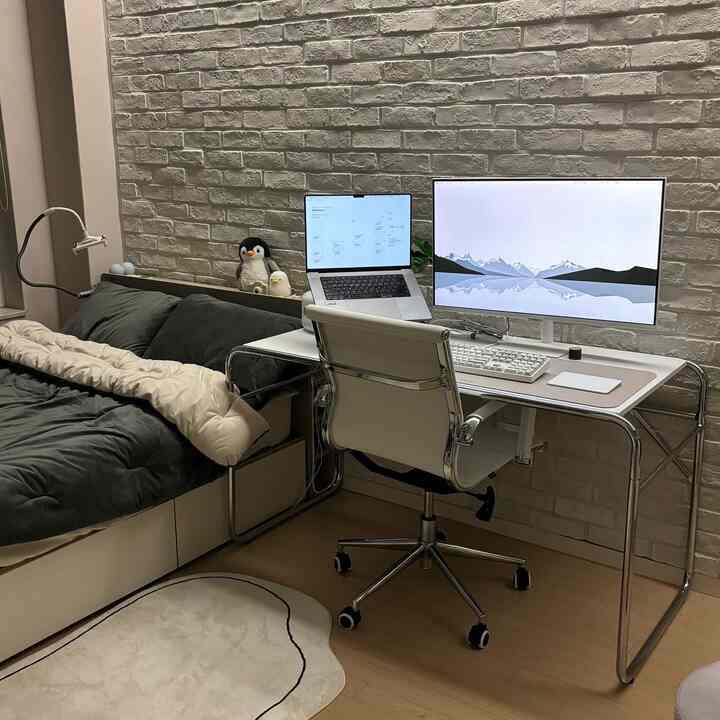 ホワイトのレンガ壁とナチュラルな木目の床が印象的な一人暮らしの部屋、モダンなデスクとソファが配置された在宅勤務用のホームオフィス空間