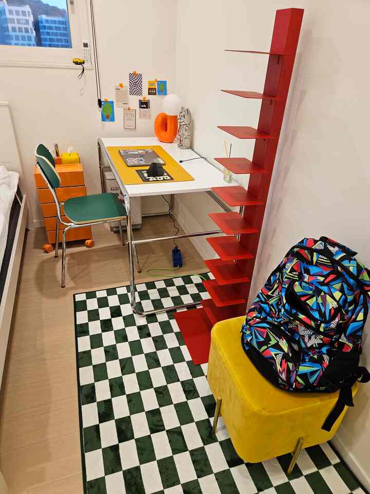 白と赤の色調の子供部屋、机と赤い棚、チェック柄のラグが配置された印象的な空間