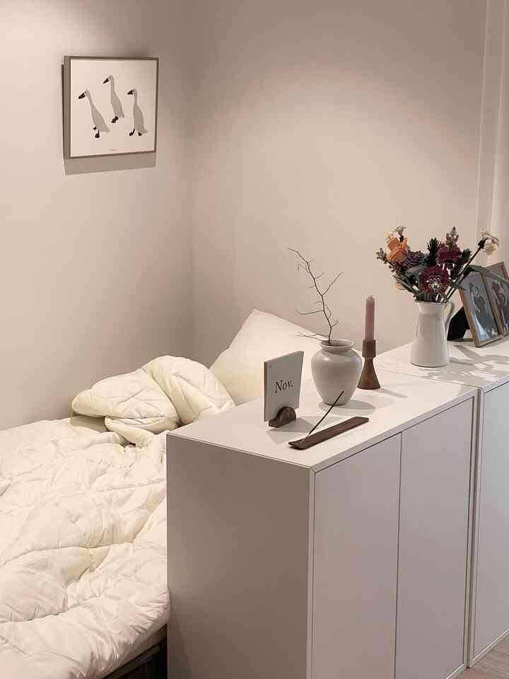 White-toned bedroom featuring a cabinet with plants and candles, showcasing a clean and modern space