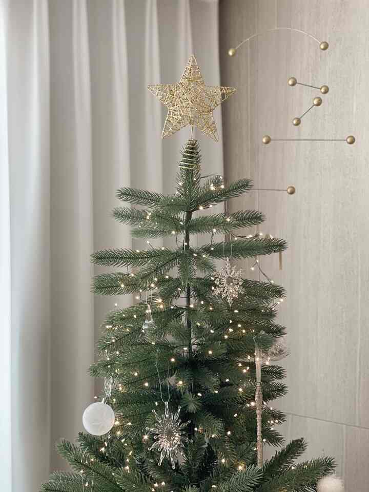 ゴールドの星とシルバーの雪の結晶オーナメントが飾られたグリーンクリスマスツリー、ベージュのカーテンを背景にした洗練された室内