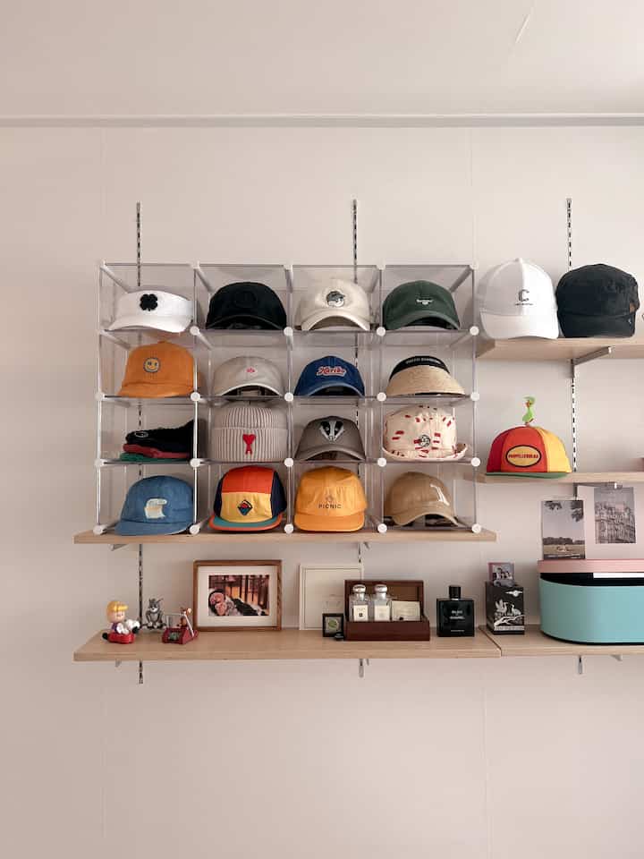 Modern walk-in closet featuring transparent acrylic hat storage and wooden wall shelves with neat, minimal décor