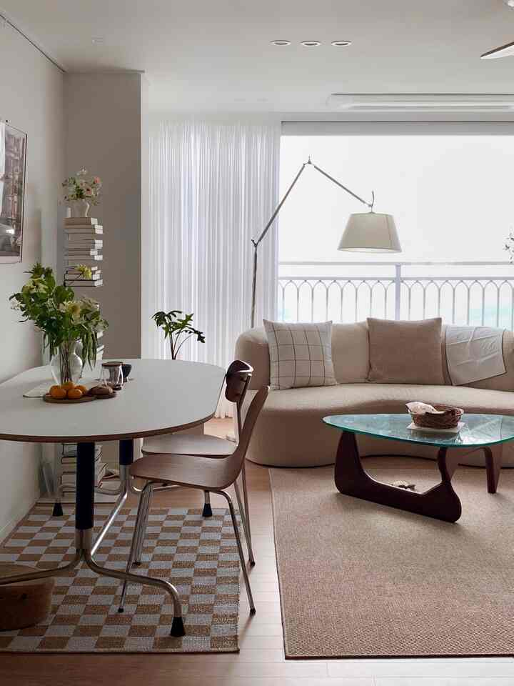 Bright beige and ivory toned living room featuring curved boucle sofa and wood-glass coffee table with simple minimalist style