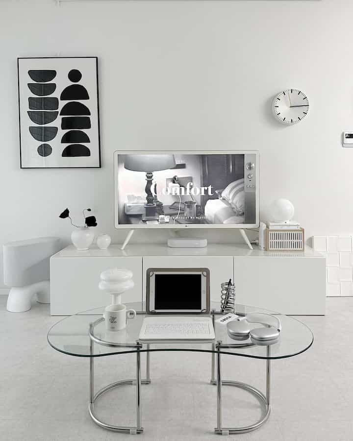 Monotone living room in white and gray tones featuring a transparent glass coffee table and tidy TV stand with minimalist decor