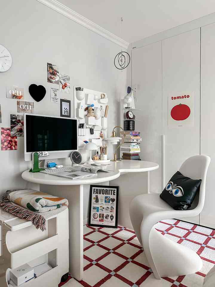 白を基調としたモダンなホームオフィス空間、丸いデスクと椅子、テーブルランプや壁の装飾が配置された清潔感のあるインテリア