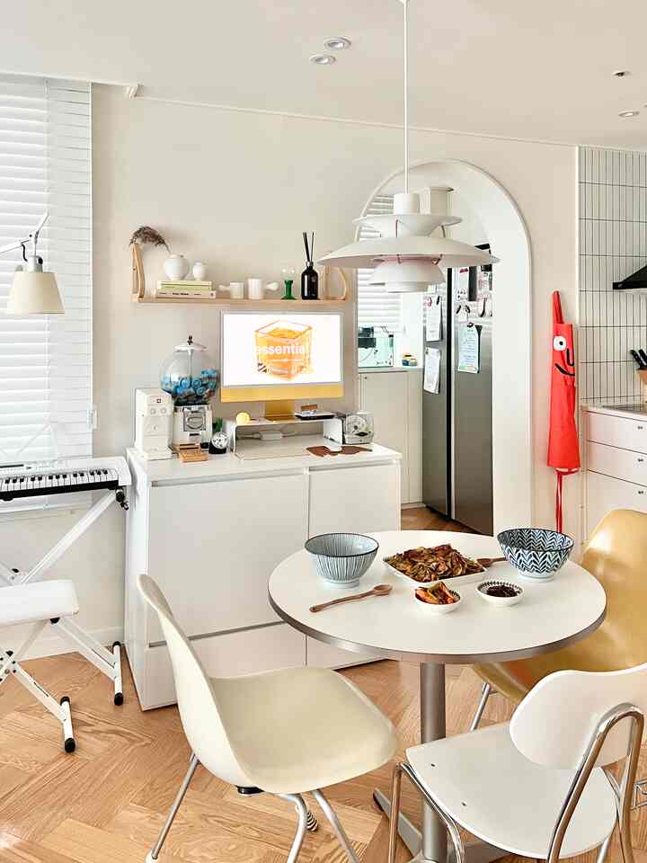 White and wood tone kitchen dining area featuring a round table with bowls, home cafe setup, and home office workspace with a calm atmosphere
