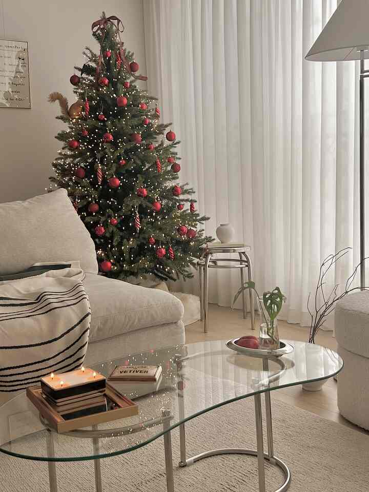 白とベージュのトーンのリビング、クリスマスツリーと透明なガラステーブルが配置された、すっきりとしたミニマルな雰囲気のインテリア