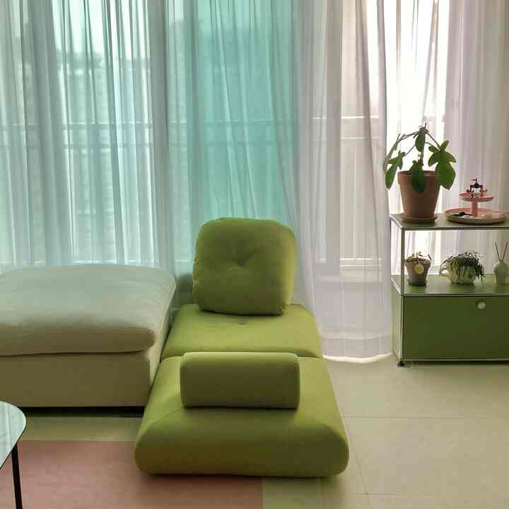 白と淡い緑の色調のリビング、モジュラーソファベッドと植物が配置された落ち着いた雰囲気のインテリア