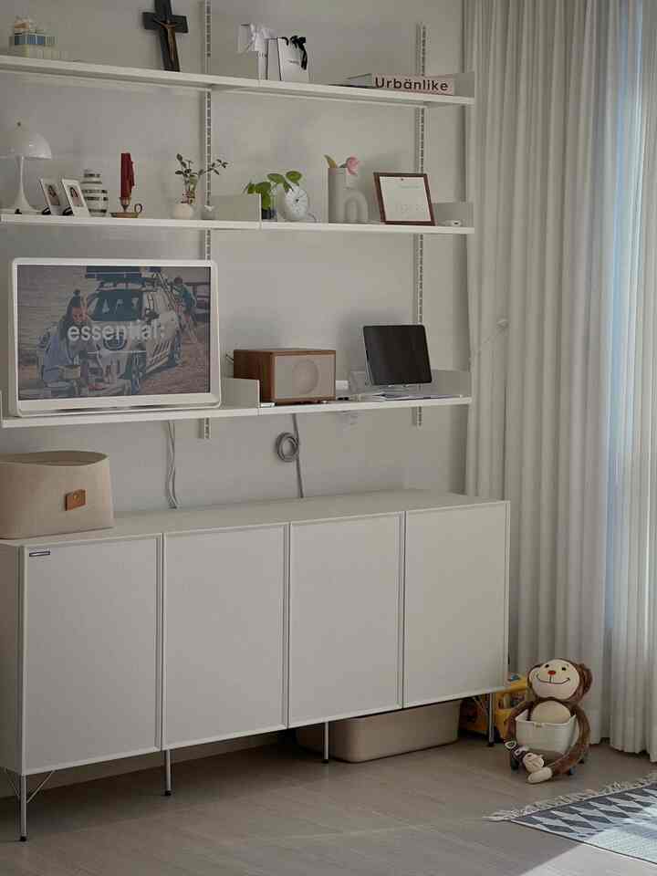 白とナチュラルな色調のリビング、壁掛け棚と収納キャビネットが配置されたシンプルで清潔感のあるインテリア