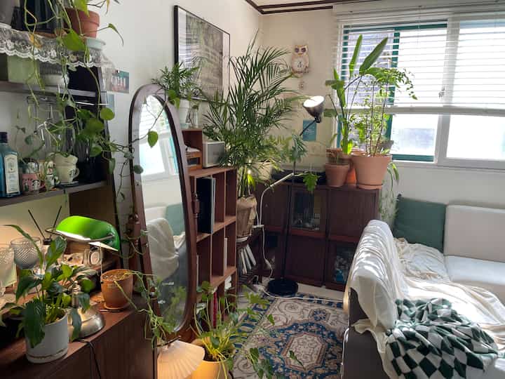 White and wood-toned L-shaped study space featuring Areca palm and various plants, creating a cozy vintage cafe-style atmosphere