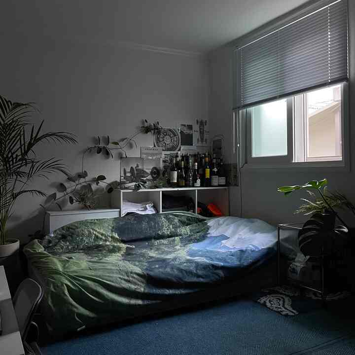 ネイビーカーペットとグリーンの寝具が配置された一人用の居心地の良い寝室、窓のブラインドとホームバーがあり、安らぎのあるインテリア