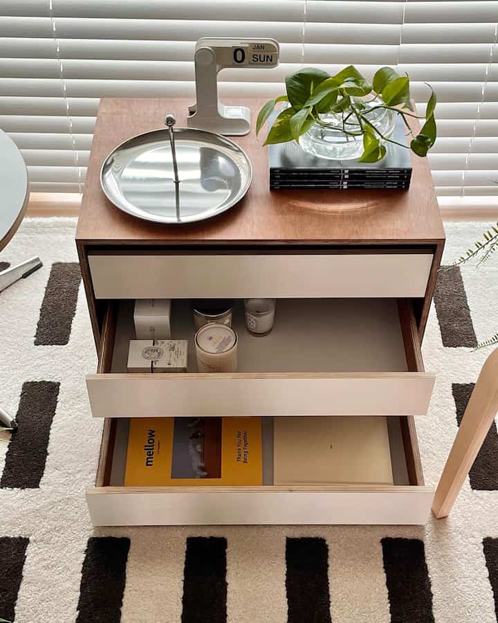 ホワイトとナチュラルトーンのリビング、木製ドレッサーとステンレストレイ、万年カレンダー、植物が配置された印象的な空間