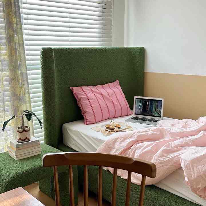 Cozy bedroom with green bed frame and pink bedding next to window with floral curtain