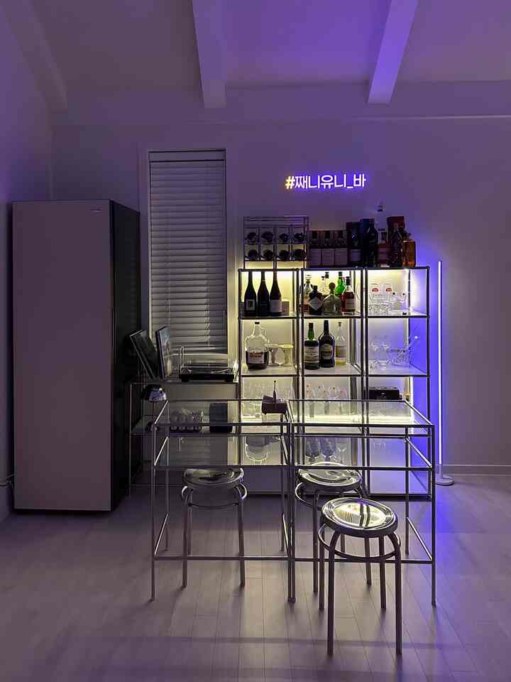 シルバーメタルとブルーネオンライトが調和するモダンなホームバー空間、ステンレススツールとガラステーブルが配置された洗練された雰囲気
