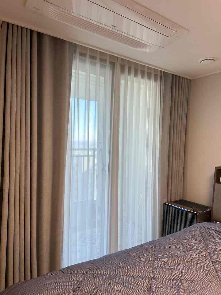 A bright bedroom in white and beige tones featuring blackout and sheer curtains covering the window with a cozy atmosphere