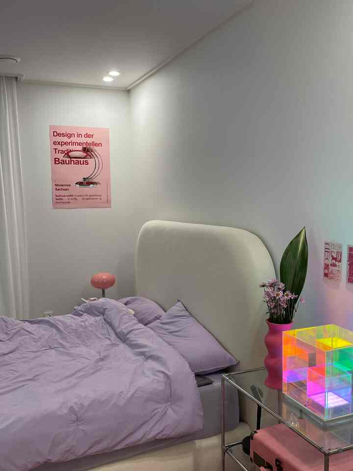 ホワイトとラベンダーの落ち着いた寝室、透明なサイドテーブルと独特な照明オブジェが配置された雰囲気のあるインテリア