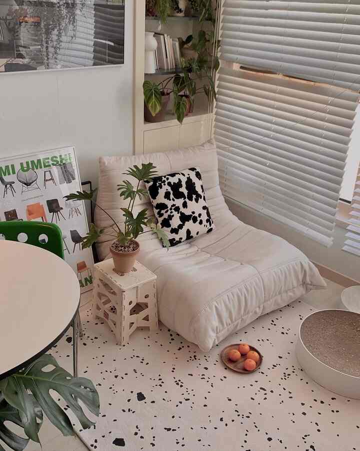 ホワイトトーンのミッドセンチュリーモダンスタイルのリビングコーナー、カウパターンクッションと観葉植物が配置された居心地の良い空間