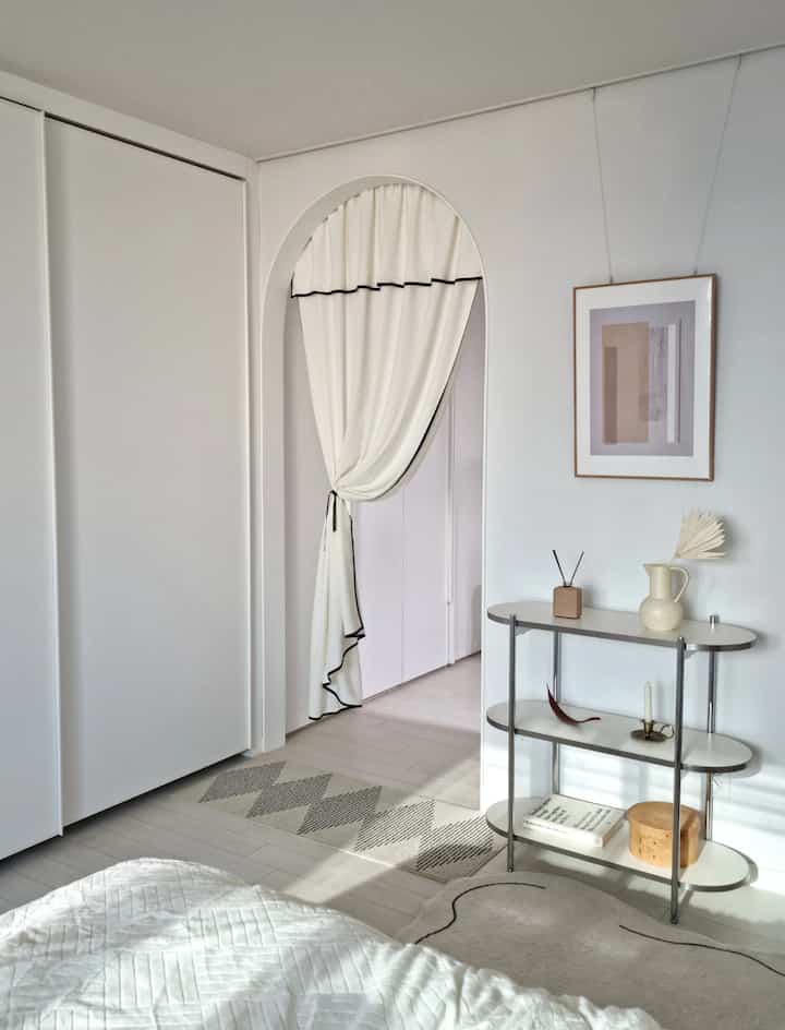 White-toned bedroom featuring an arched doorway and simple shelving with natural wood flooring, creating a clean and calming atmosphere