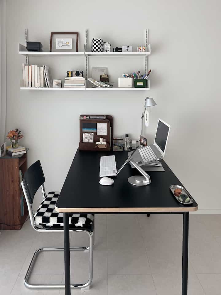 A simple and modern study with white walls and a black desk, featuring tidy desk storage and a table lamp