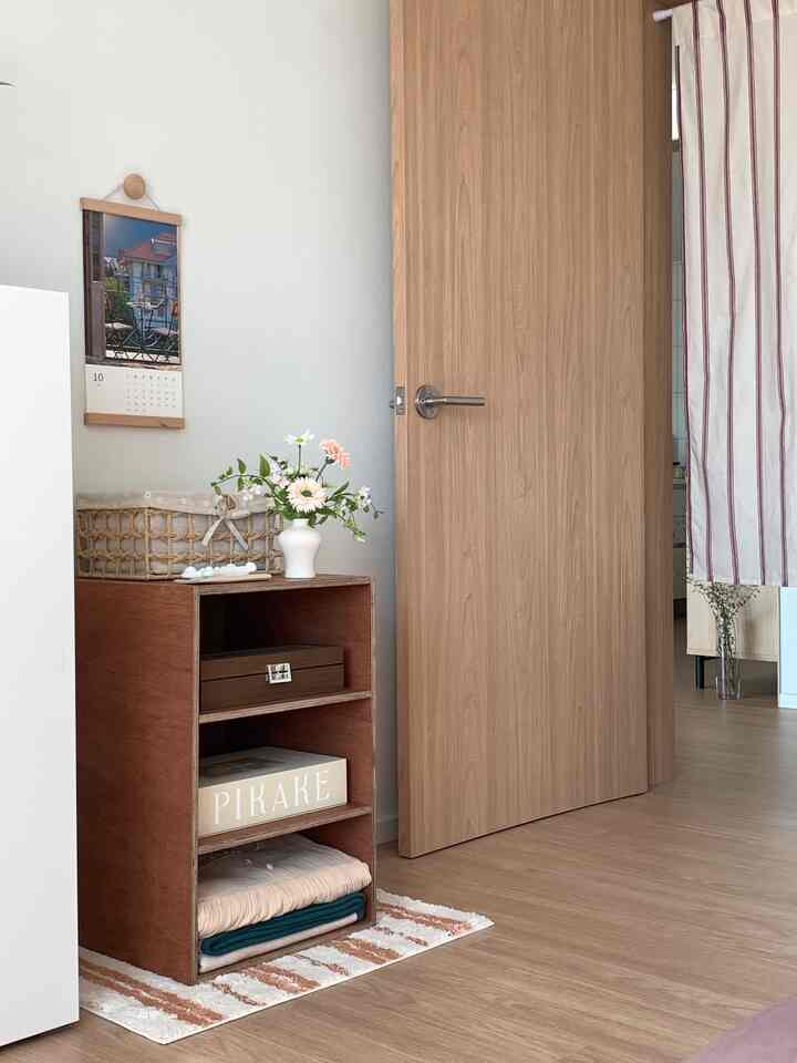 Natural wood tone bedroom corner featuring a small open storage cabinet beside a wooden door, creating a cozy and neat atmosphere