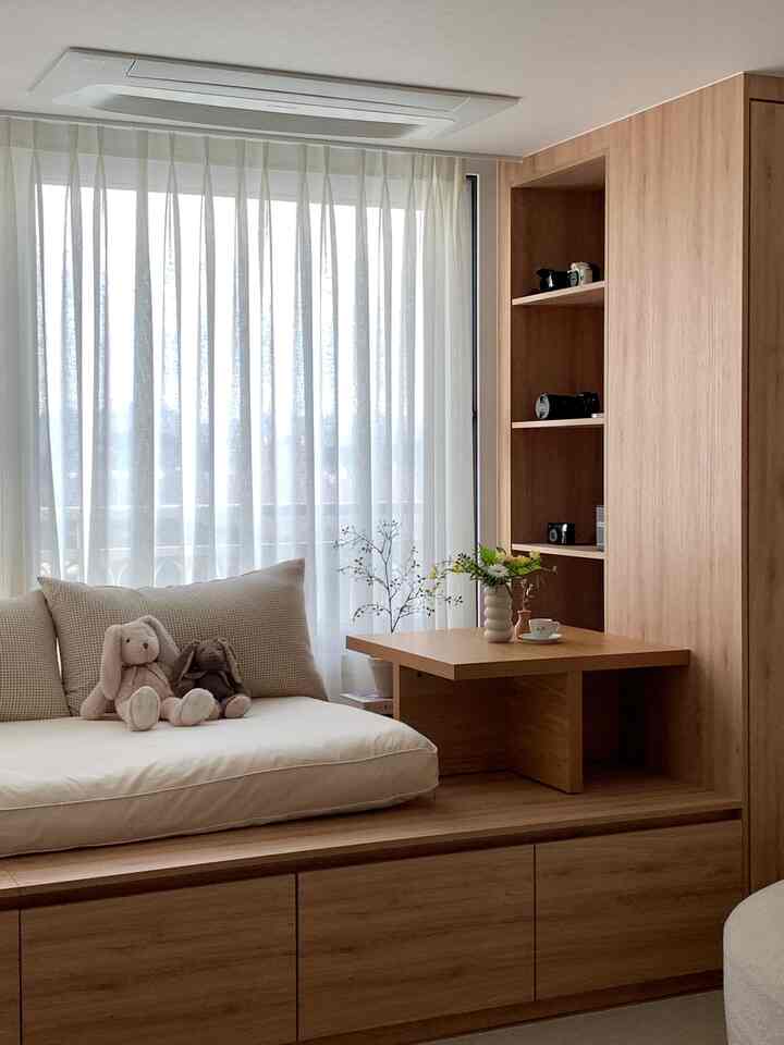 ナチュラルなブラウンの木目調が特徴的なリビング、ベージュのソファとカーテンが落ち着いた雰囲気を演出