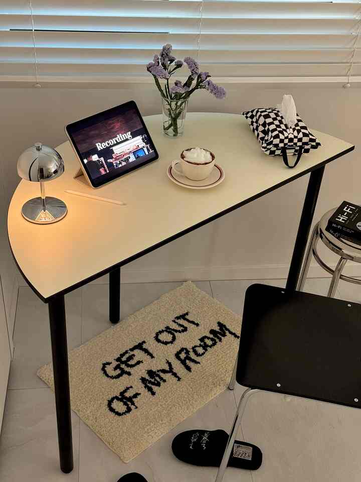 White-toned compact home office space featuring a rounded desk with an iPad and table lamp, exuding a cozy mood