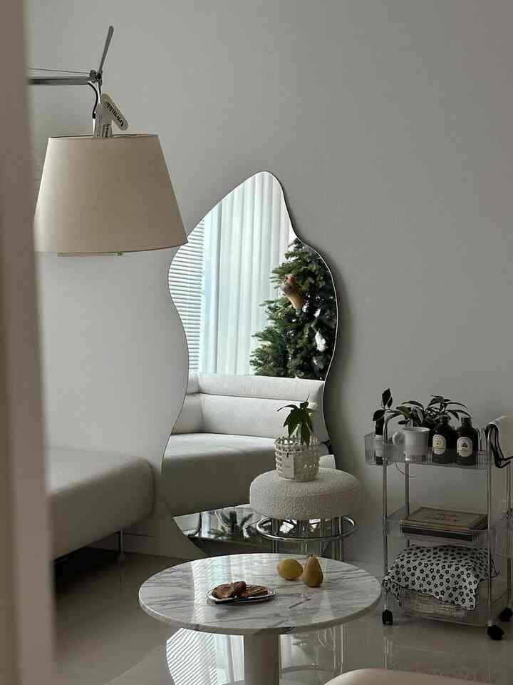 白を基調としたリビング、透明アクリルの3段トロリーと特徴的な形の全身鏡を配したモダンでミニマルなインテリア