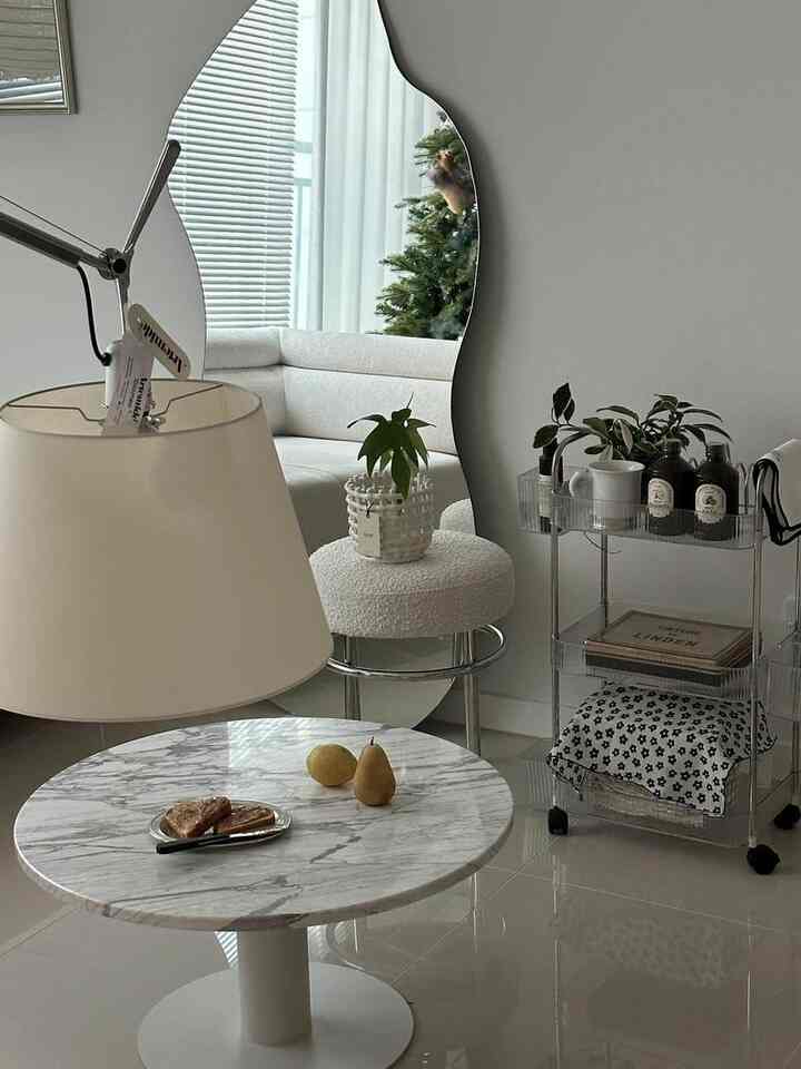 白と透明なアクリルが調和するリビング、3段移動式トロリーと大理石のコーヒーテーブルが配置されたモダンでナチュラルな空間
