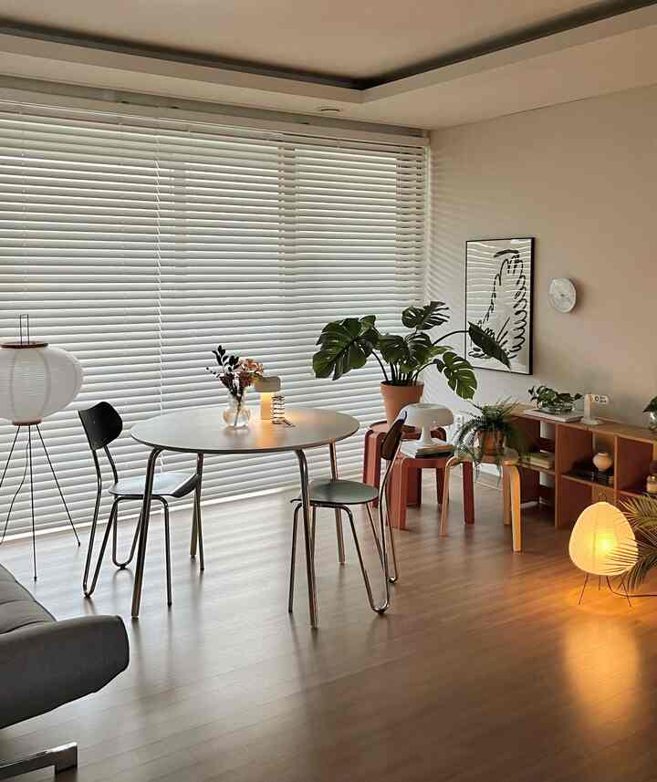 Bright living room with light brown wood floor, a round table and blinds creating a simple, natural atmosphere