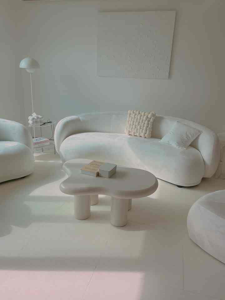 白を基調としたリビング、曲線形のソファと独特な形のコーヒーテーブルが配置されたシンプルでモダンな空間