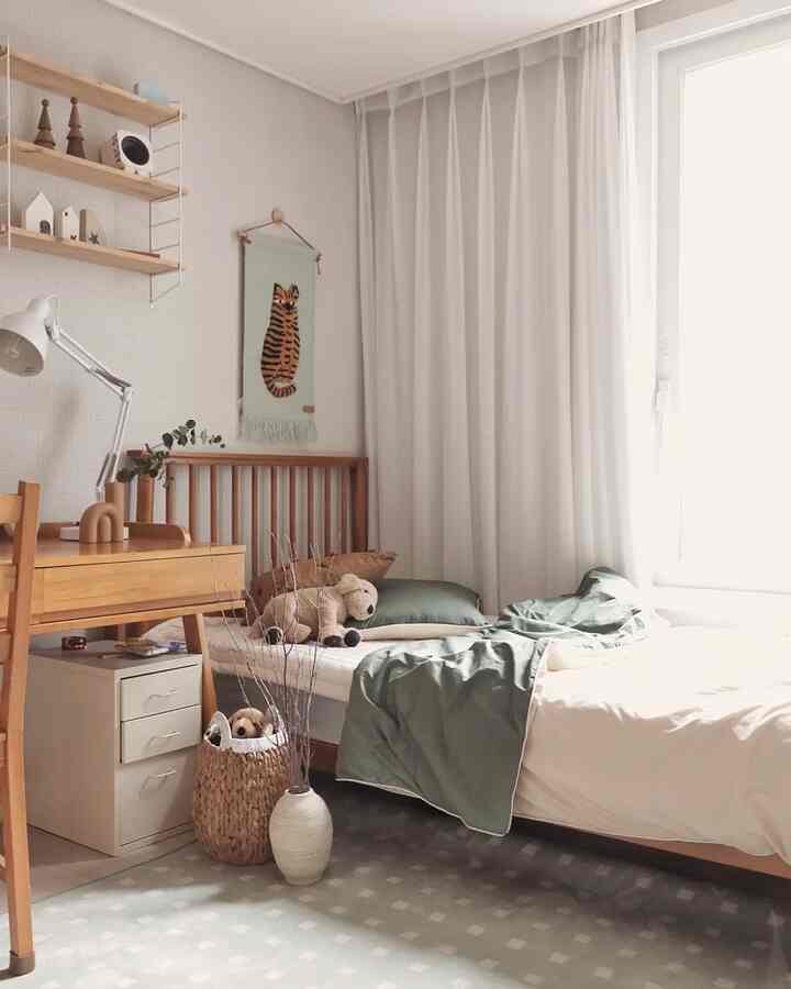 Warm wood tones and white curtains in a kids' room featuring a children's desk and bed with a natural, cozy atmosphere