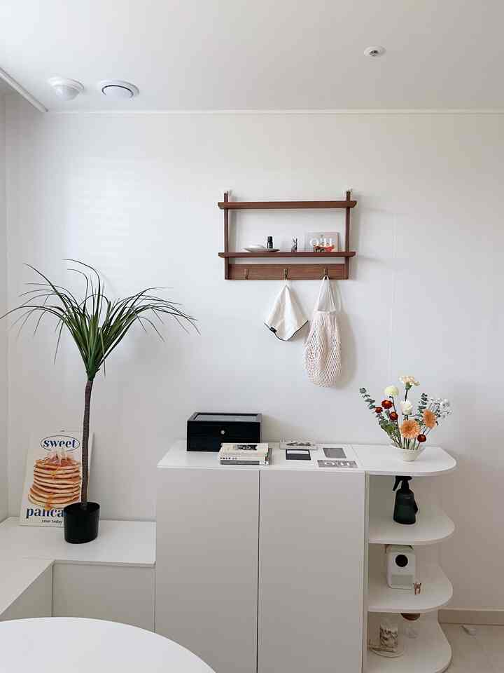 白とナチュラルカラーを基調とした玄関、木製の壁棚と植物が配置されたシンプルで清潔感のあるインテリア