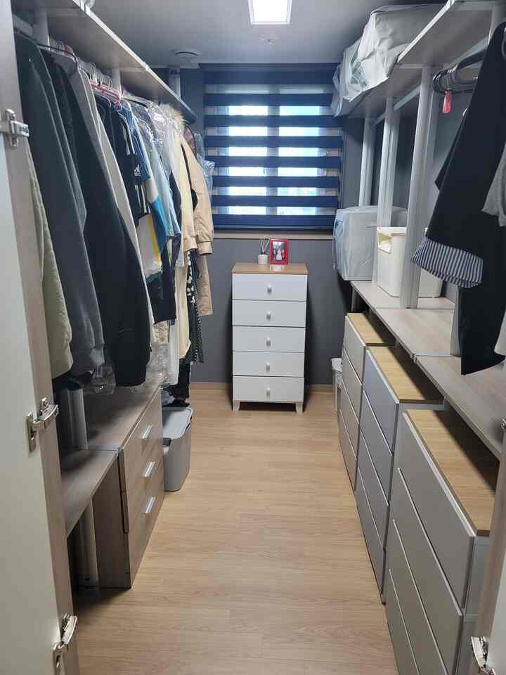 ナチュラルな木目調と白いチェストが配置された細長いウォークインクローゼットの空間