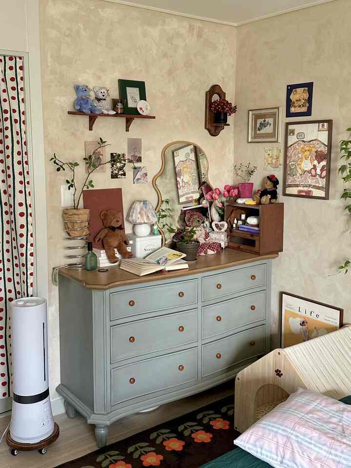 Cozy bedroom with warm ivory-toned walls and blue dresser, decorated with teddy bears, vanity mirror, and vintage decor