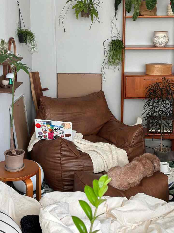 ナチュラルなブラウンの木目調とクリーム色のテキスタイルが調和するロフトのワンルーム、ビーズクッションソファと植物が配置された雰囲気のある空間