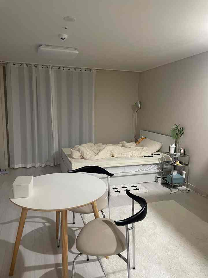 ベージュとホワイトのトーンの1人用寝室、丸いテーブルとシンプルなインテリアが特徴的な温かみのある空間