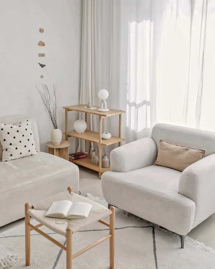 A white and wood tone living room featuring a comfortable sofa and natural stool arranged in a cozy setting