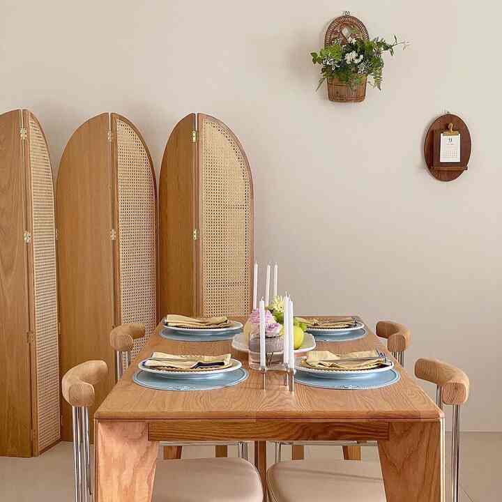 A simple dining room with natural wood tones and rattan partitions, featuring placemats and candles creating a cozy atmosphere