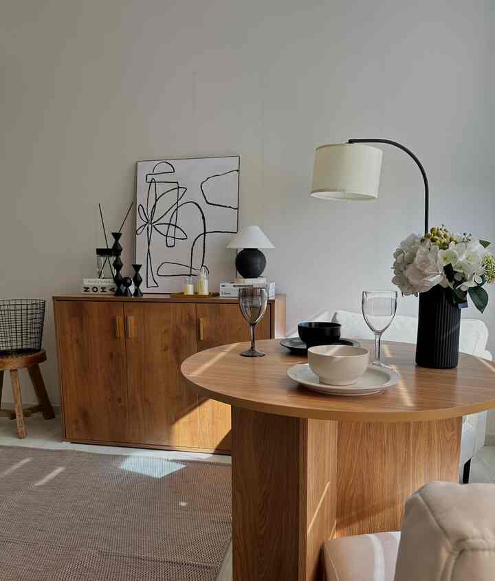 ナチュラルモダンな色調のリビング、丸い無垢材のダイニングテーブルとサイドボード、フロアランプが配置された清潔感のある空間