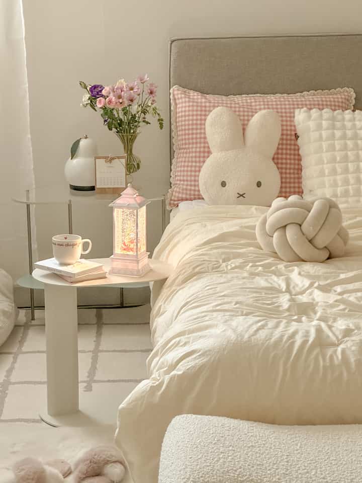 Beige headboard and cream bedding with checkered cushion and bunny plush in white-toned bedroom interior