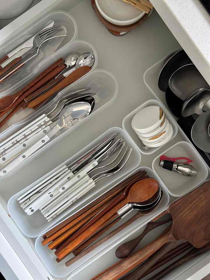 A white and wood tone kitchen drawer neatly organized with cutlery in a clean space