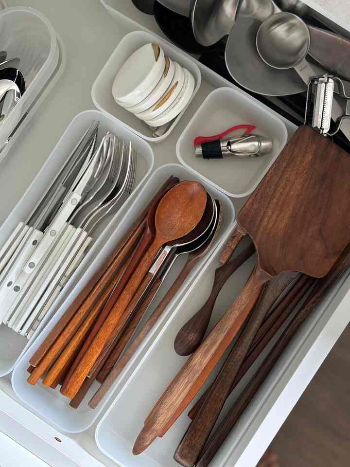 Kitchen drawer with white plastic organizers neatly holding wood-toned spoons and cutlery arranged by type
