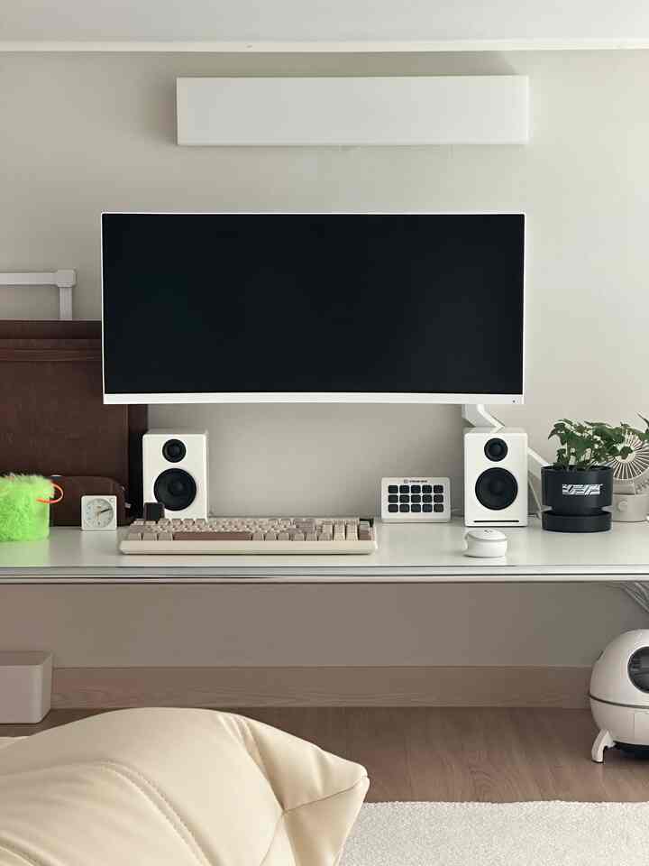 A compact home office space with white and wood tones, featuring a curved monitor and audio speakers in a tidy workspace