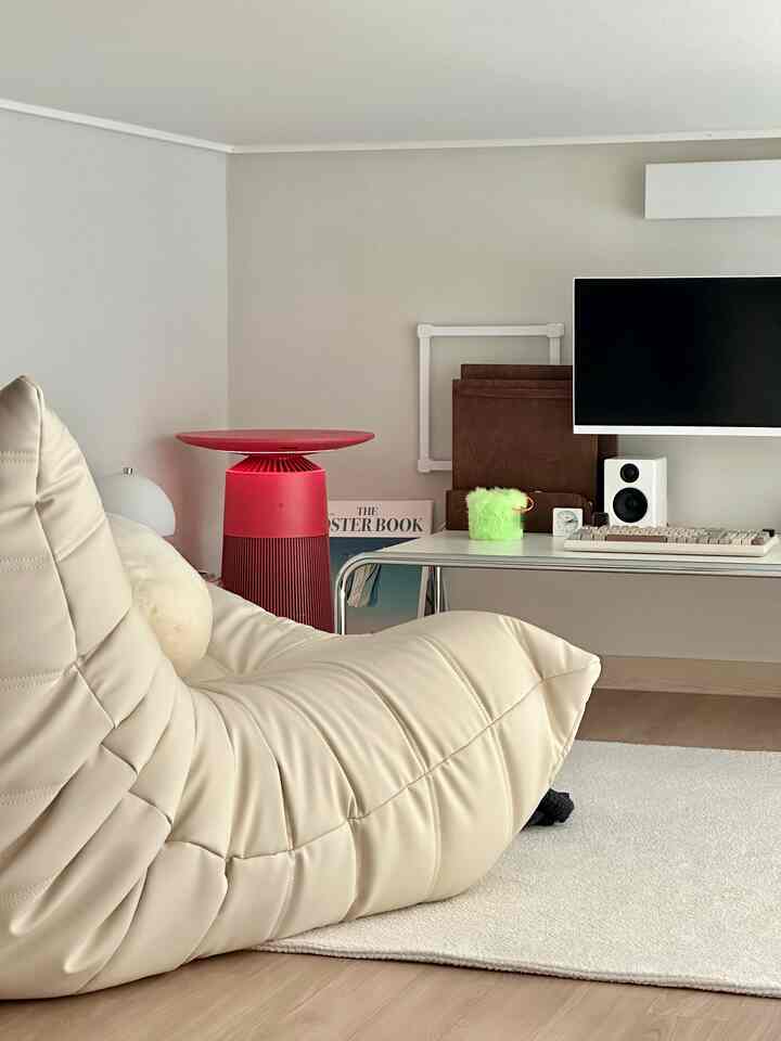 Beige-toned living room featuring a large faux leather sofa, wall-mounted TV, and a minimalistic home office setup with a clean modern style