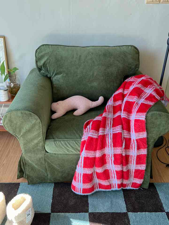 緑色のアームチェアに赤いチェック柄のスローとピンクのクッションが置かれた、雰囲気のあるリビングスペース