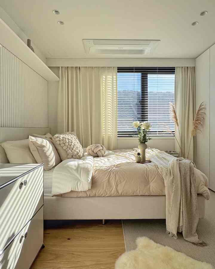 ベージュとアイボリーの色調の寝室、ベージュの寝具と多様なクッション、サイザルラグとウールラグが温かみのある自然な雰囲気を演出