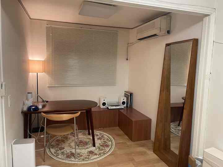 木目調と白いブラインドが調和したシンプルモダンなリビング、デスクとスツール、フロアランプが配置された居心地の良い空間